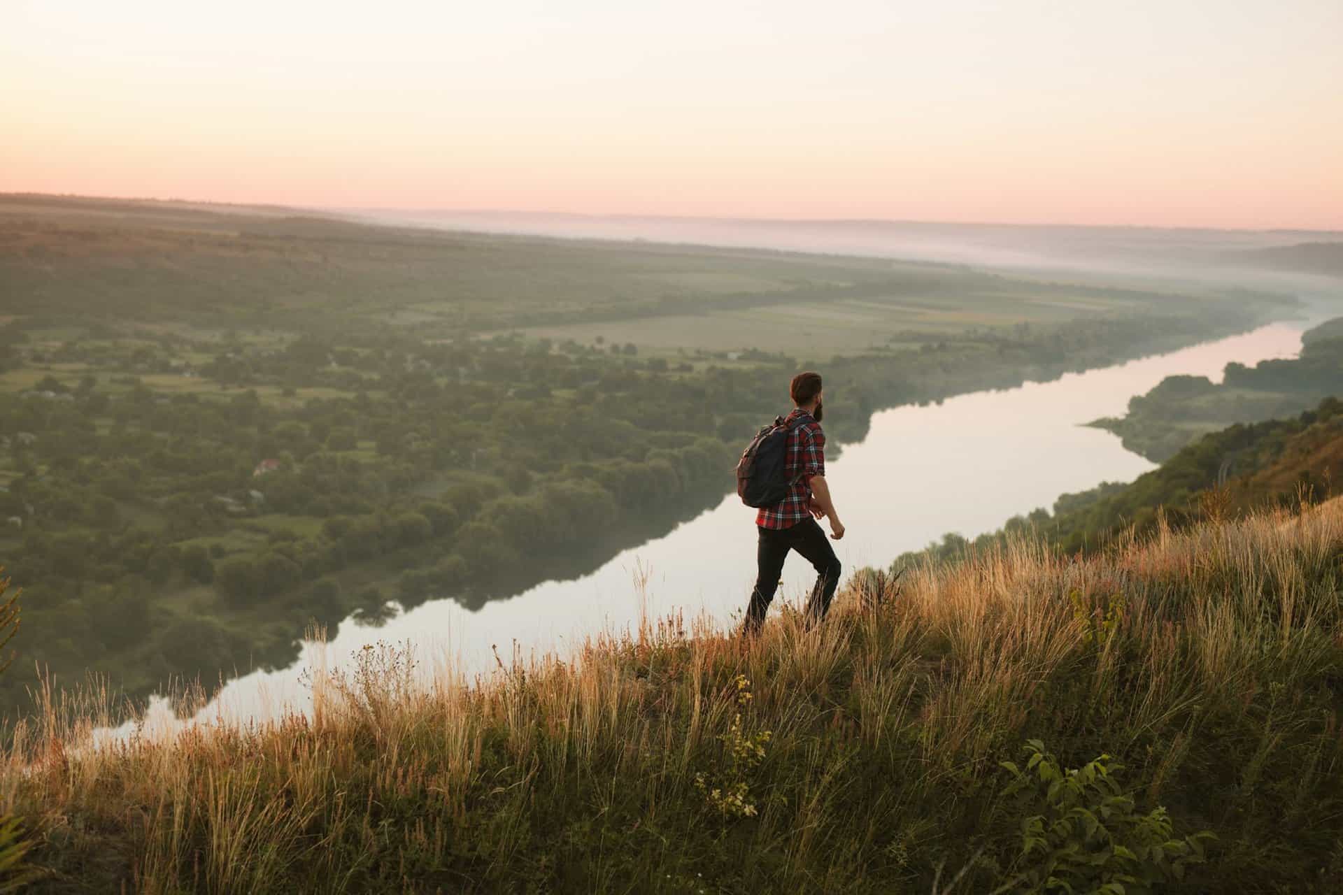 Male hiker walking on hill near river