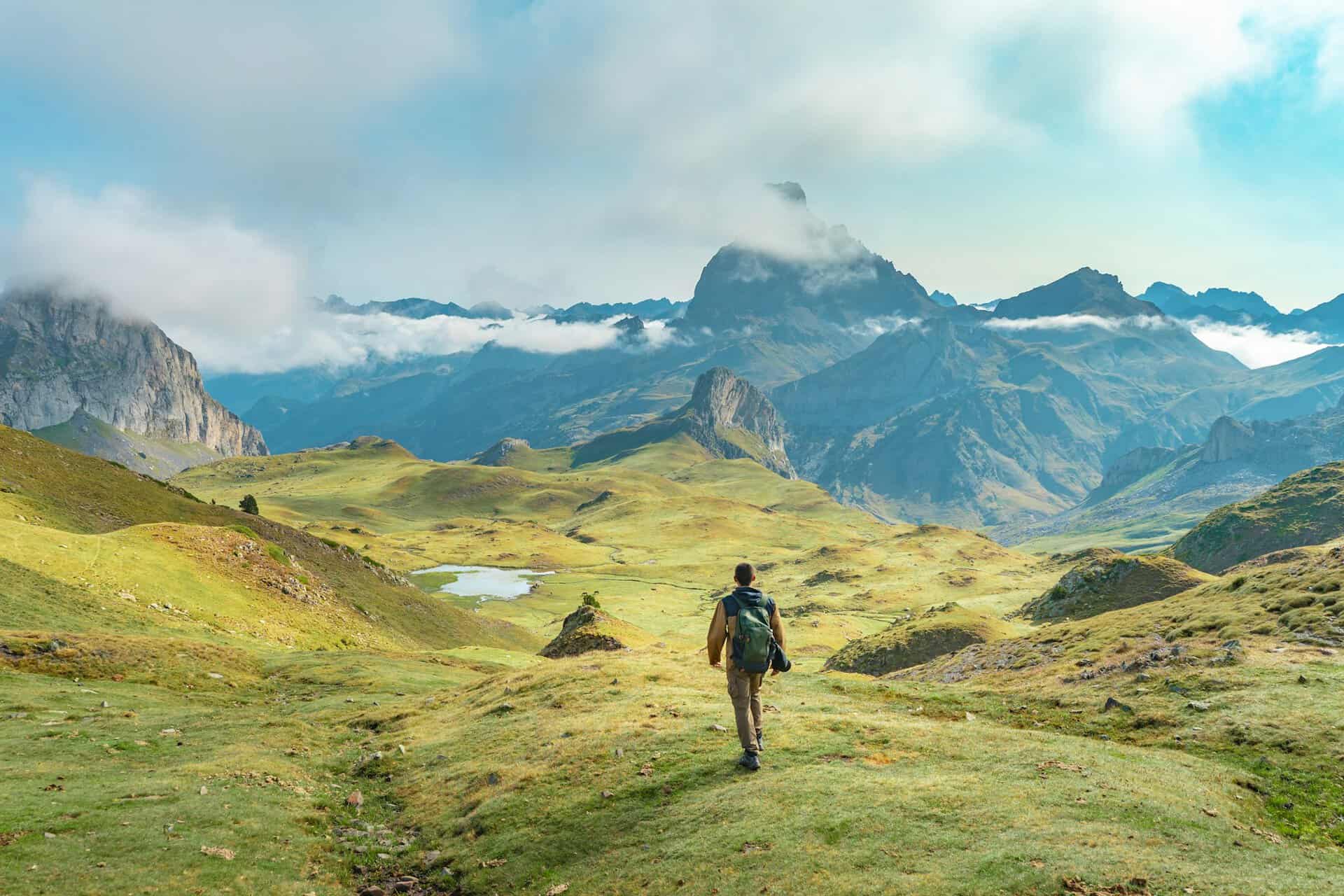 Young man is walking up a grassy hill in the mountains under a cloudy sky